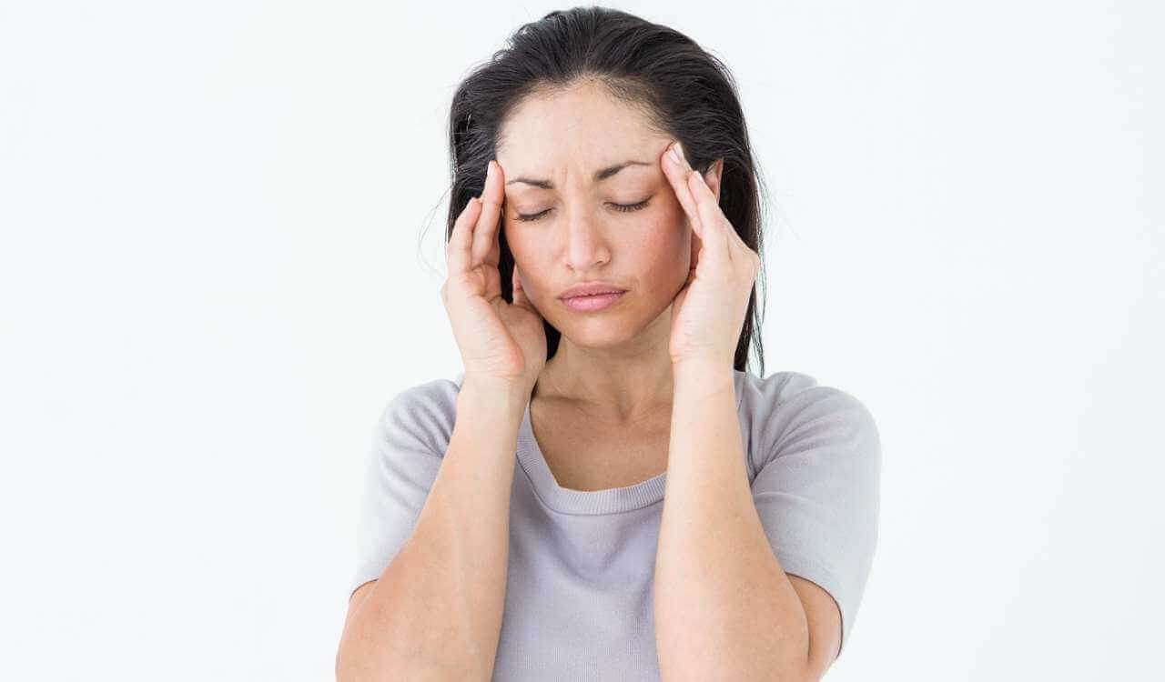 Eine Frau mit schmerzverzerrtem Gesicht hält die Hände an die Schläfen. Wie hilft Akupressur und das Liegen auf einer Akupressumatte bei Migräne?